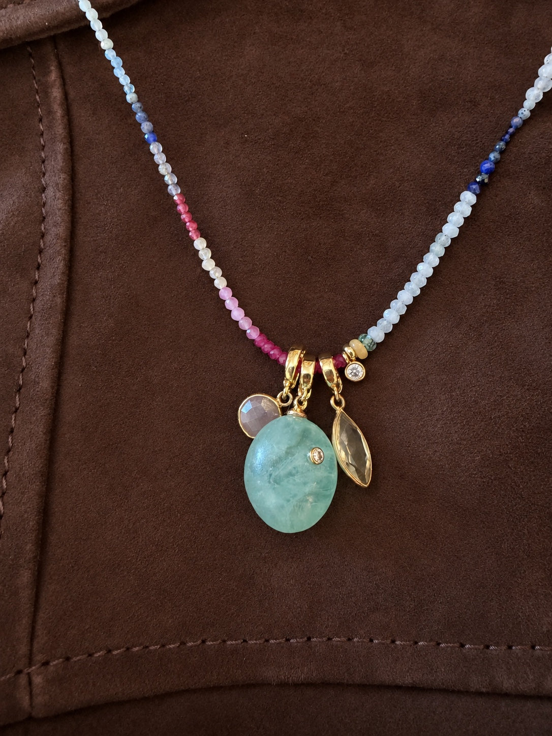 Vela Relic paired with other Relics on a gemstone strand over brown suede