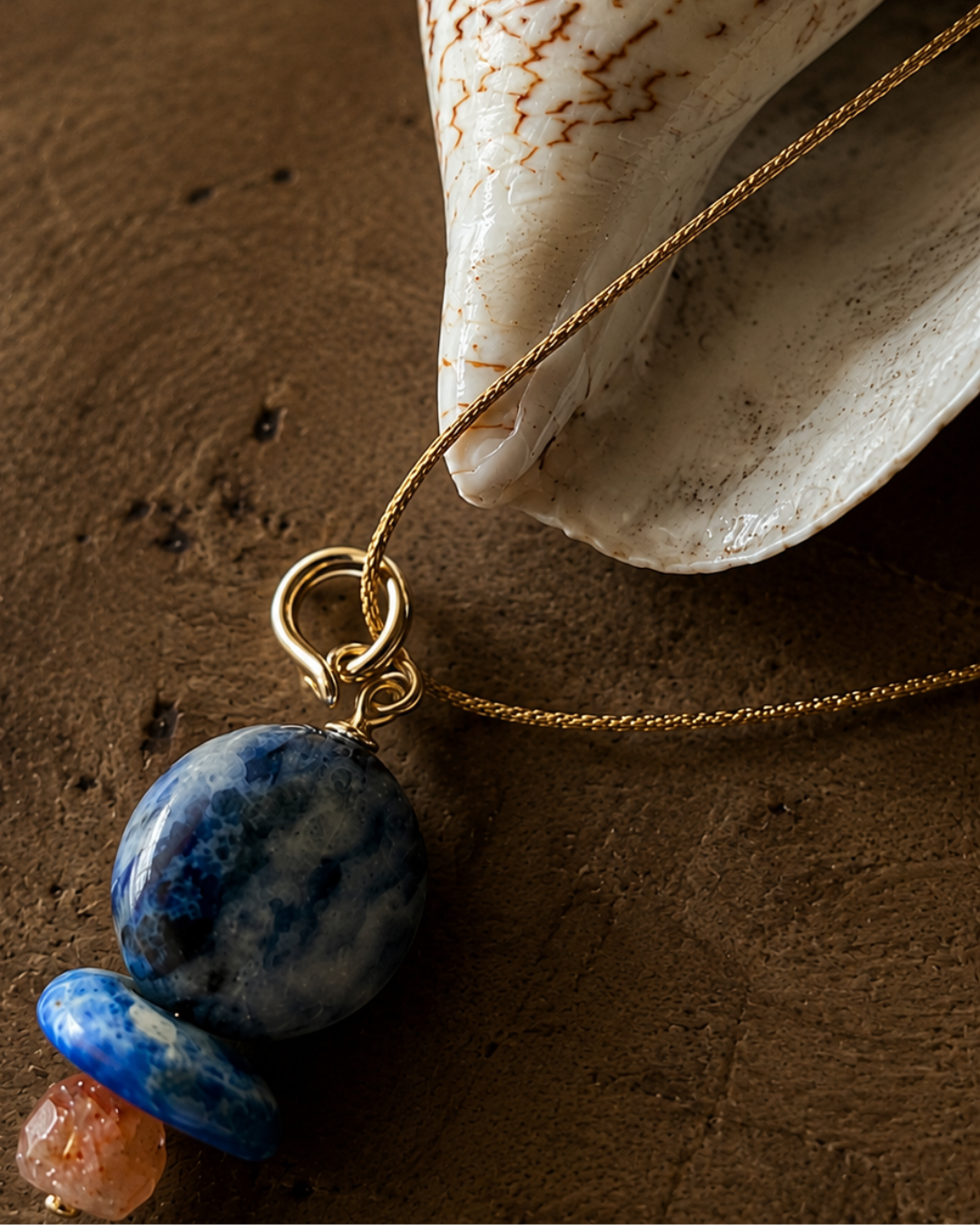 close up of lapis pendant on metallic cord and part of a shell