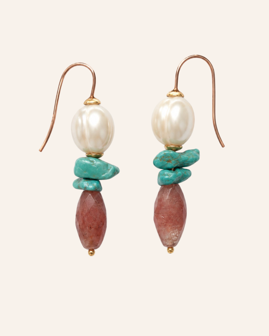 A pair of bohemian-style dangle earrings featuring a white baroque pearl, turquoise chips, and a reddish-brown stone bead, suspended from gold hooks on a light beige background.