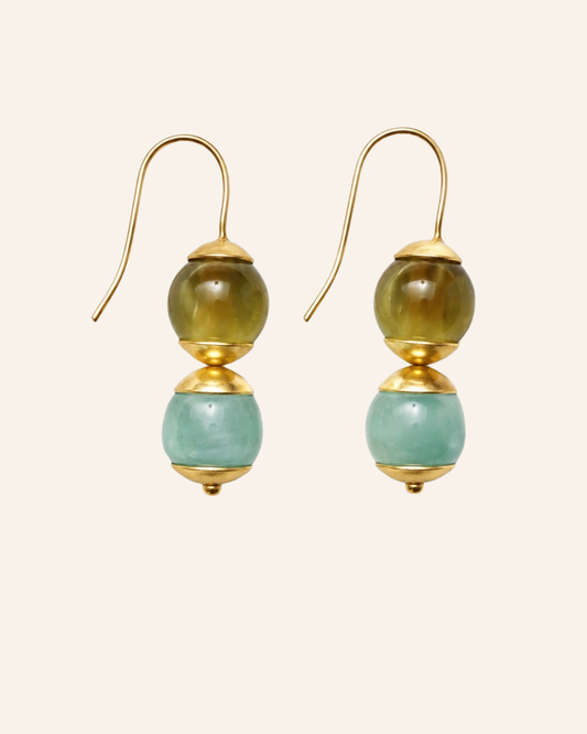 A pair of gold-tone dangle earrings with two stacked round beads, one olive green and one light aqua blue, shown on a plain light beige background.
