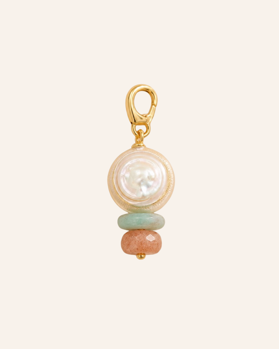 A gold charm featuring a round white pearl, a light green stone bead, and a peach-colored stone bead, set against a solid pale cream background.