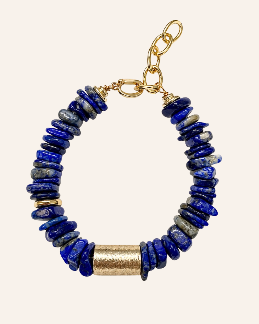 A beaded bracelet featuring dark blue lapis lazuli stones, a textured gold cylinder bead, and gold chain clasp on a light beige background.