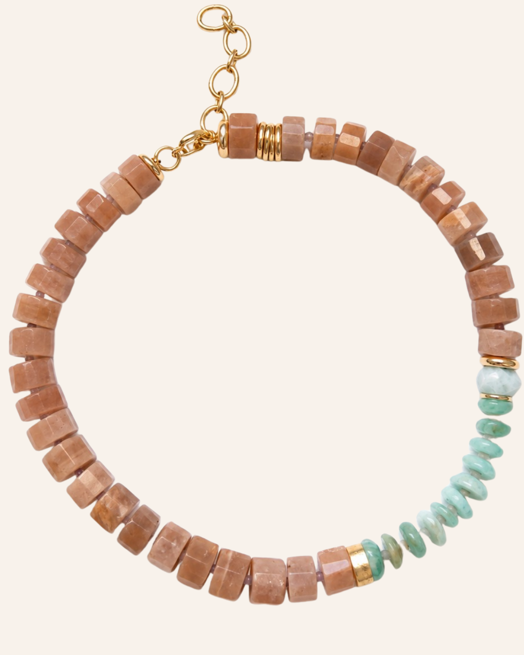 A beaded necklace featuring faceted light peach moonstonebeads and a section of polished light green gemstone beads, finished with gold-toned metal spacers and a gold clasp on a light beige background.