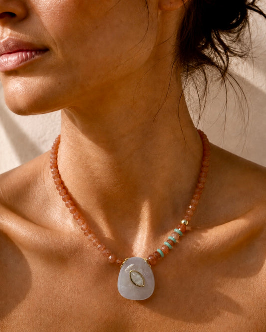 A close-up of a woman wearing a beaded necklace with a large white teardrop pendant featuring a small gold crescent moon detail.