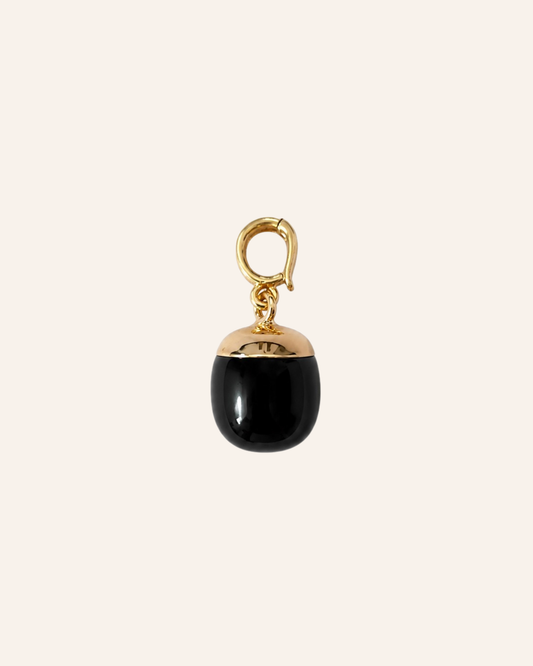 A small gold-tone jewelry charm or pendant with a black glossy dome-shaped drop and a gold lobster clasp, centered on a light cream background.