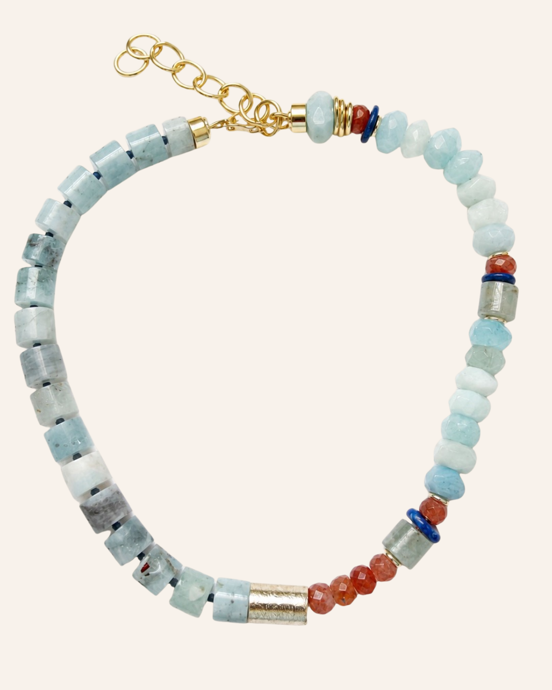 A beaded necklace featuring light blue and white stone beads, small red-orange beads, silver-toned cylindrical spacers, and a gold-toned chain clasp, displayed on a solid pale pink background.