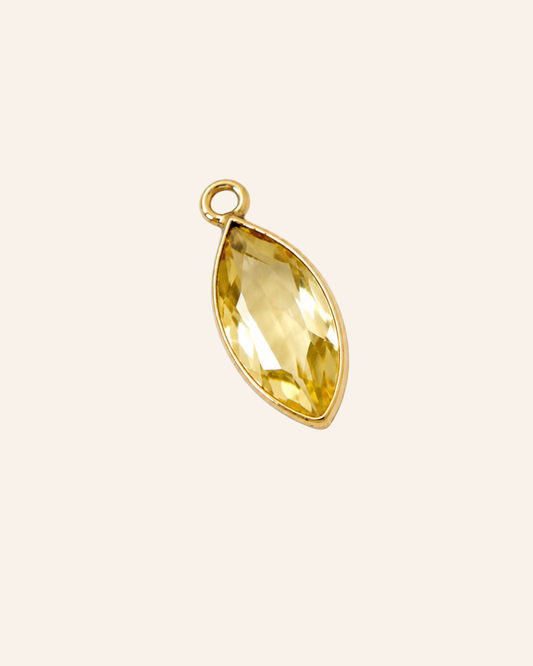 A gold leaf-shaped pendant charm featuring a faceted yellow gemstone, shown on a solid pale pink background.