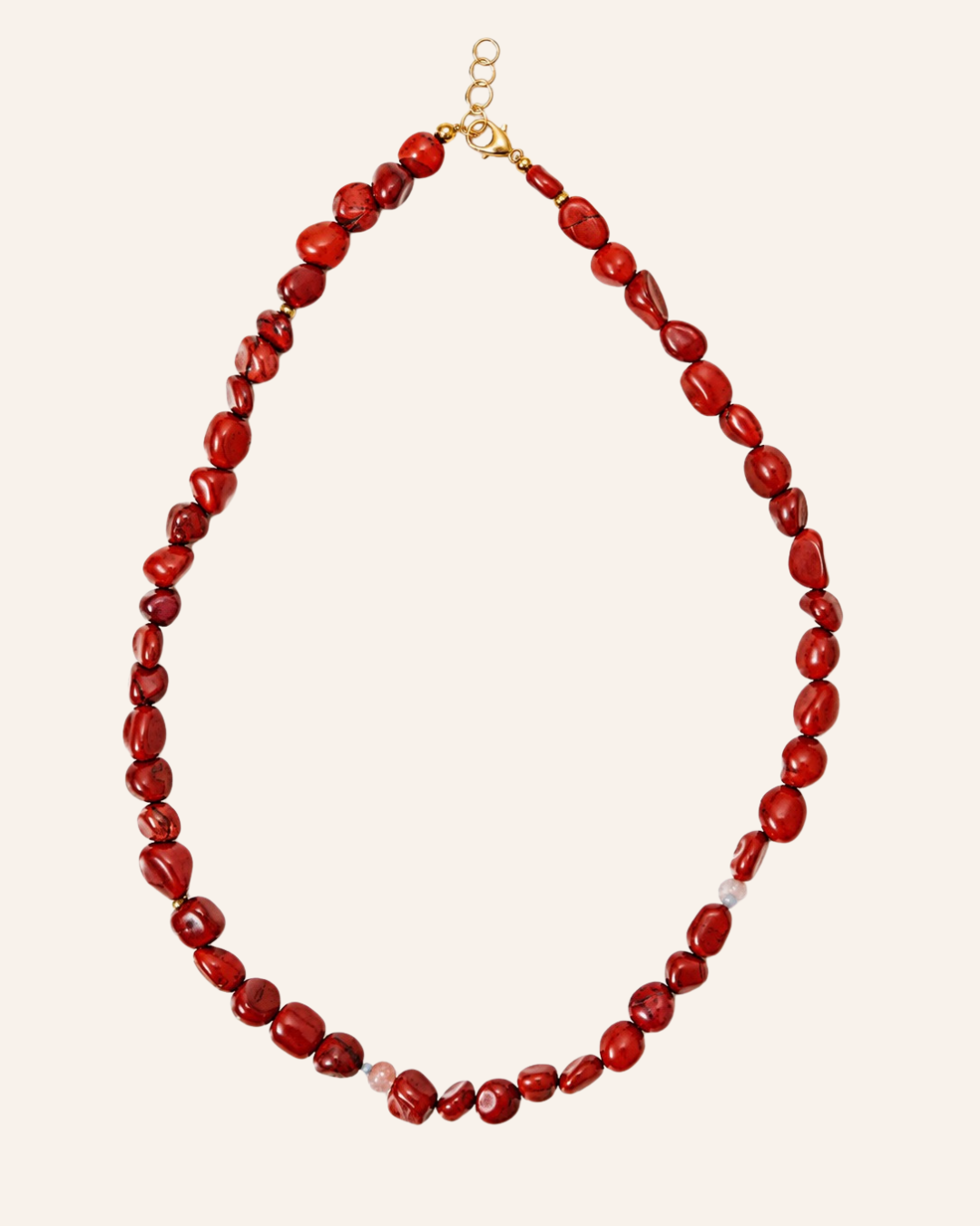 A beaded necklace made of irregular, faceted red beads with a small gold clasp, displayed on a solid light beige background.