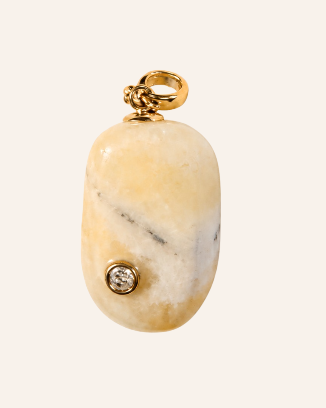 A gold pendant featuring a polished, rounded cream and white marble cabochon with a small bezel-set clear gemstone, shown against a solid off-white background.