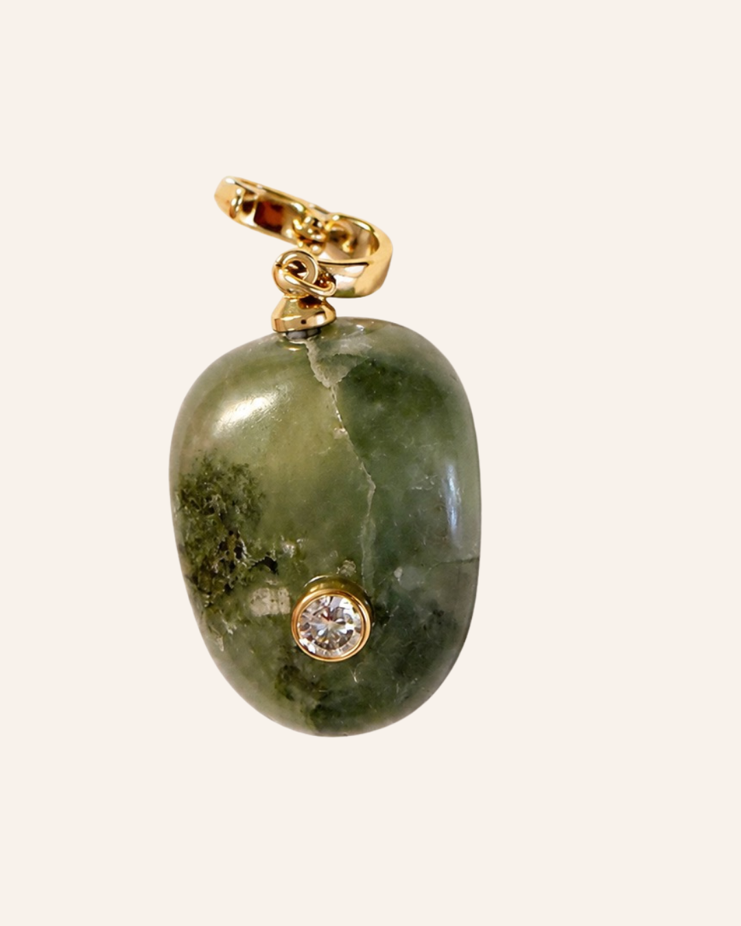 A green stone pendant with natural marbling and a small gold bezel-set clear gemstone, attached to a gold bail, shown on a light cream background.