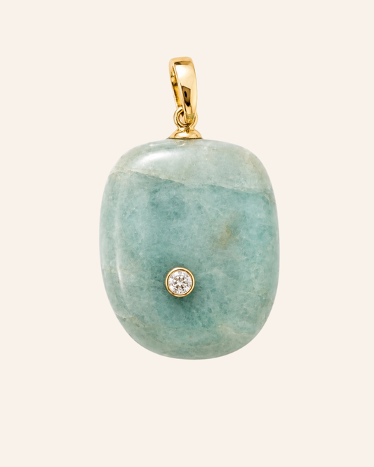 A polished light green stone pendant with a small gold bezel-set clear gemstone, suspended from a gold bail, shown against a solid pale beige background.