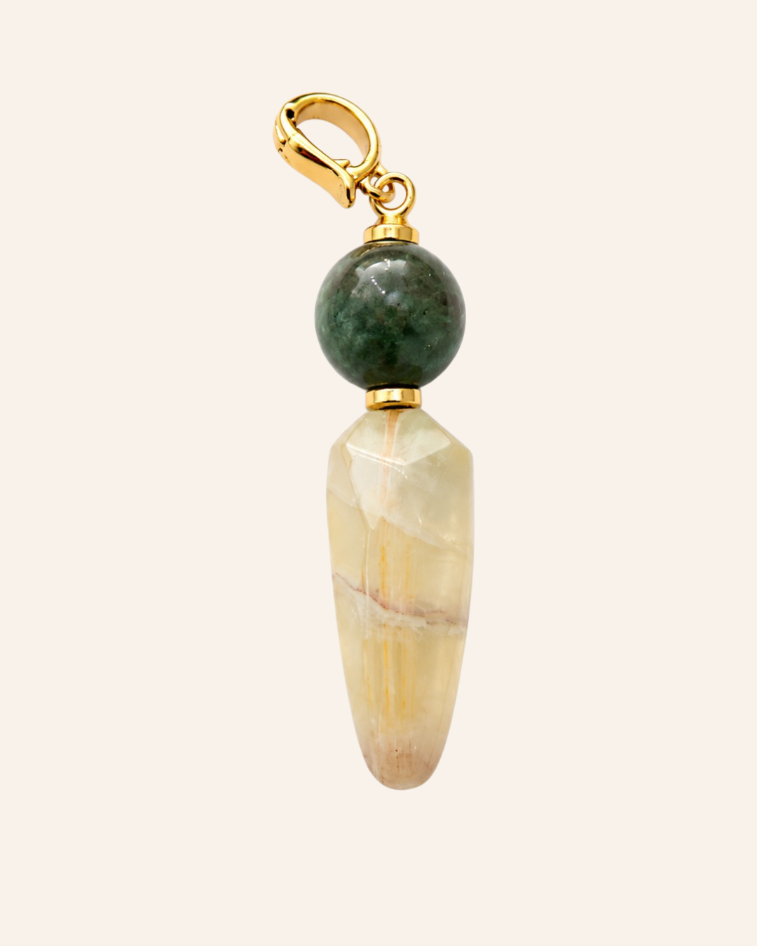 A handmade pendant charm featuring a faceted cream-colored stone cone, a polished dark green bead, and a gold-tone lobster clasp, set against a solid pale pink background.