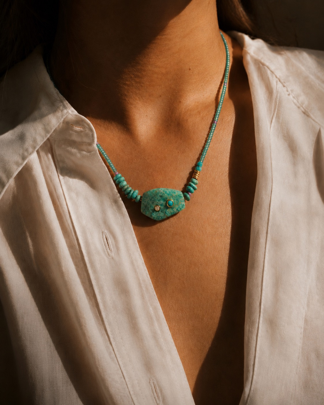 Person wearing a turquoise necklace with a plain background