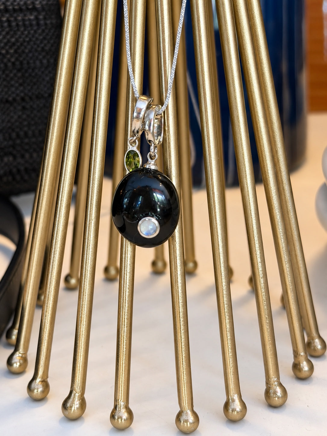 Noa Relic suspended on a silver chain against a sculptural brass stand